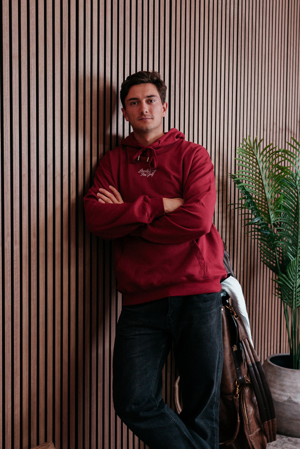 Burgundy hoodie worn leaning against a slatted wall