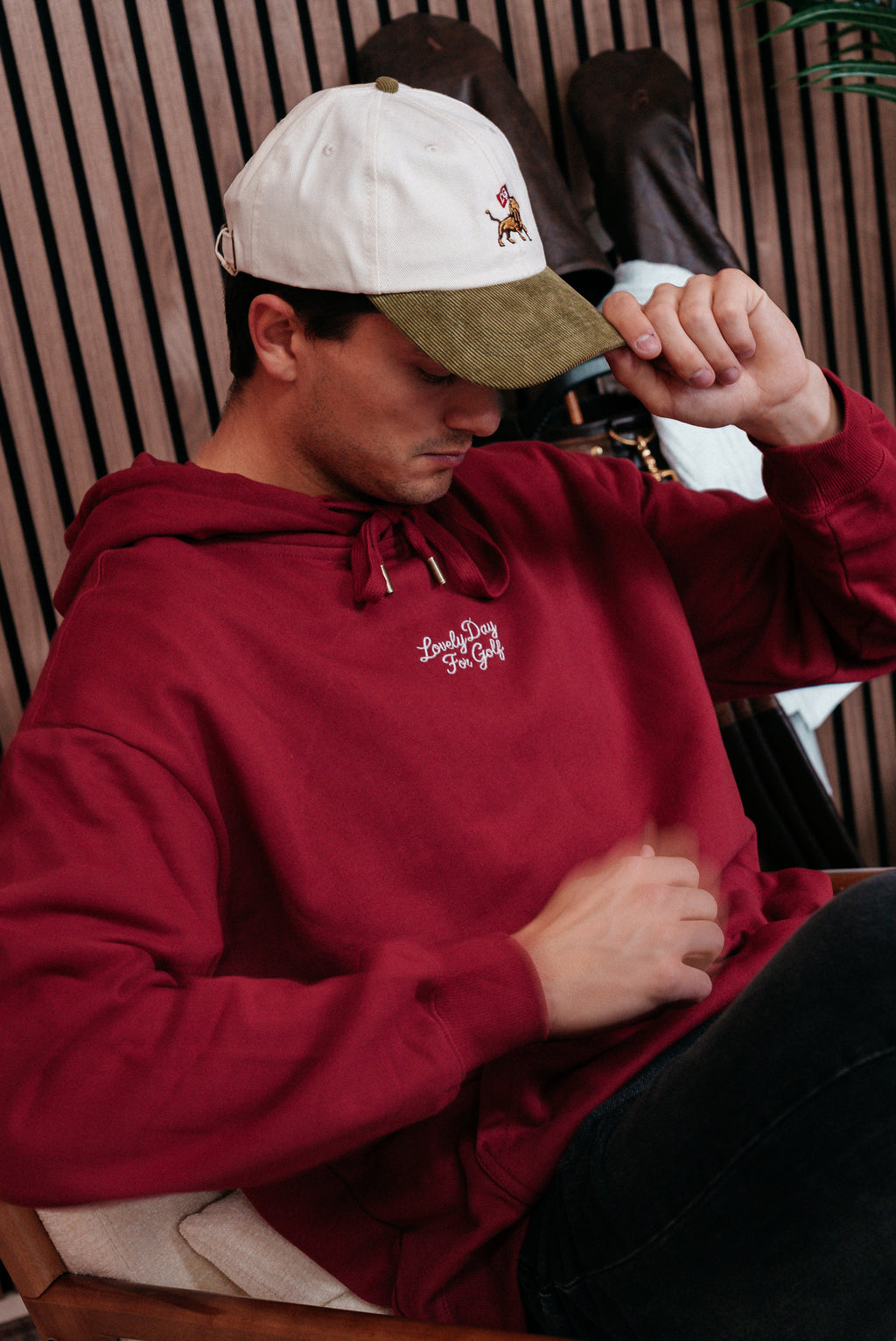Burgundy hoodie worn seated with a cream cap